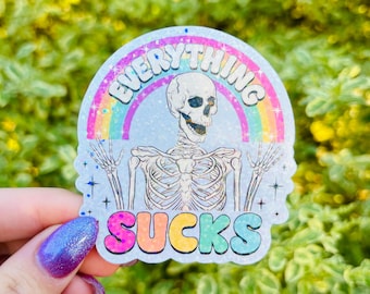 Può includere: Un adesivo con un arcobaleno e uno scheletro con il testo "Everything Sucks" in lettere colorate.