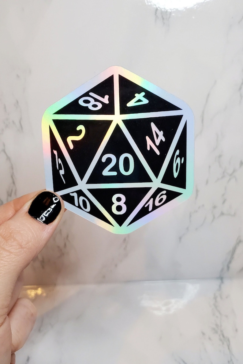 May include: A black and holographic D20 sticker with white numbers. The sticker is in the shape of a twenty-sided die, used in tabletop role-playing games. The numbers are clearly visible against the black background.