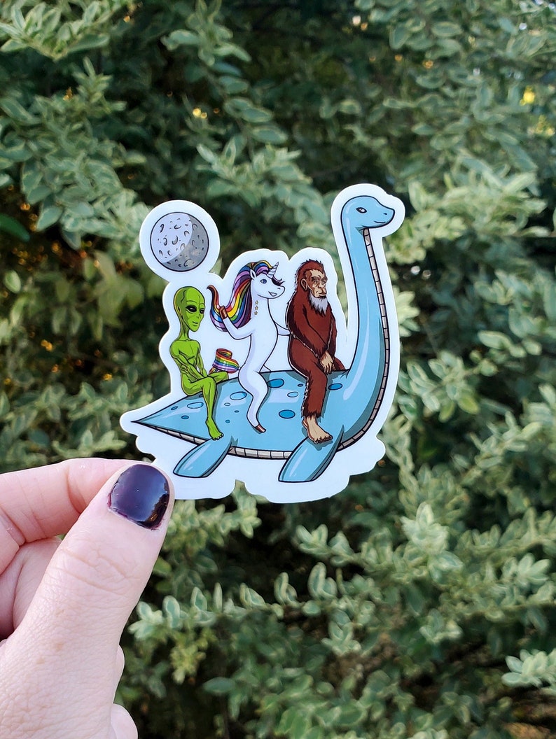 May include: A sticker featuring a blue dinosaur with a green alien, a unicorn, and a bigfoot riding on its back. The dinosaur is facing right and has a long neck. The unicorn is white with a rainbow mane and tail. The alien is green with large eyes. The bigfoot is brown and hairy. The sticker is on a white background.