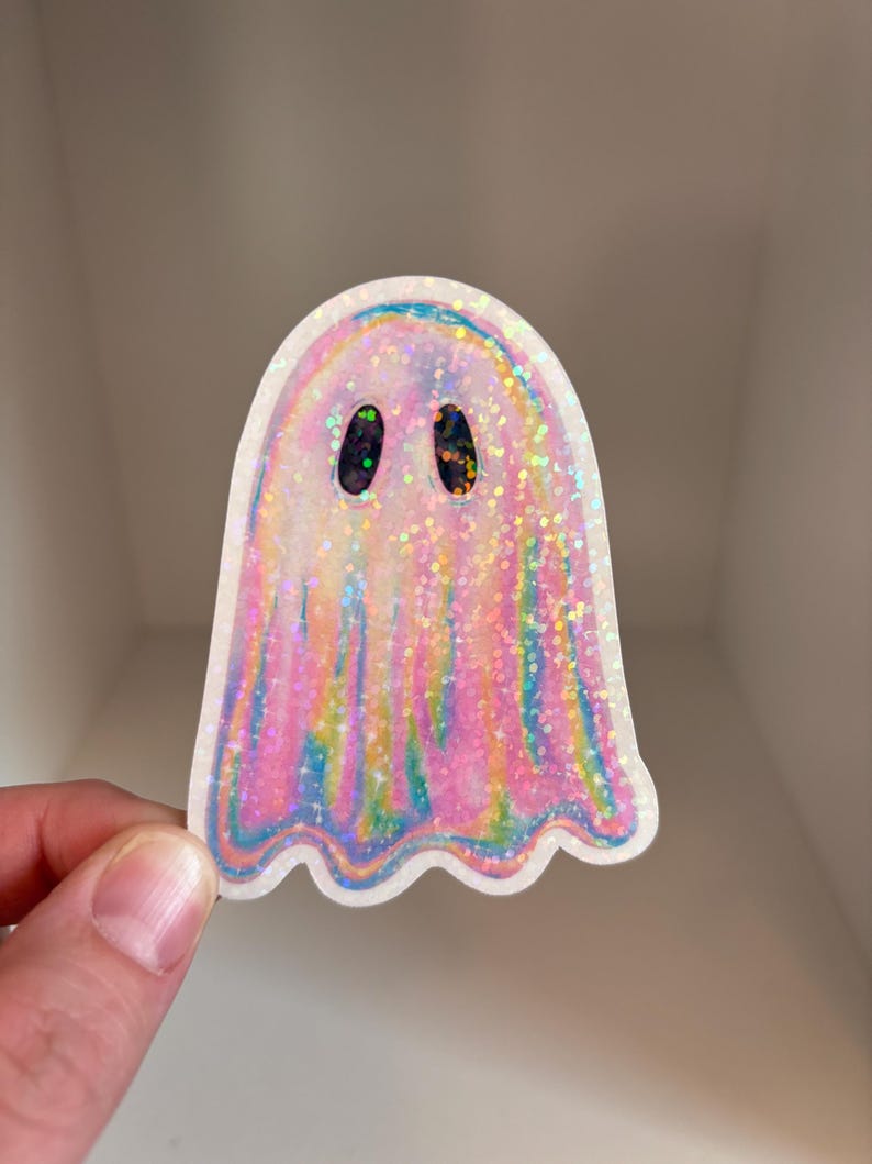 K&ouml;nnte beinhalten: Ein holografischer rosa und blauer Glitzer-Geisteraufkleber mit schwarzen Augen.