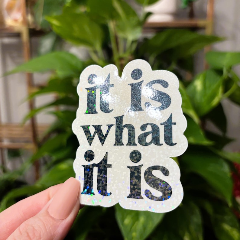 May include: White sticker with iridescent glitter and black text that reads "it is what it is".