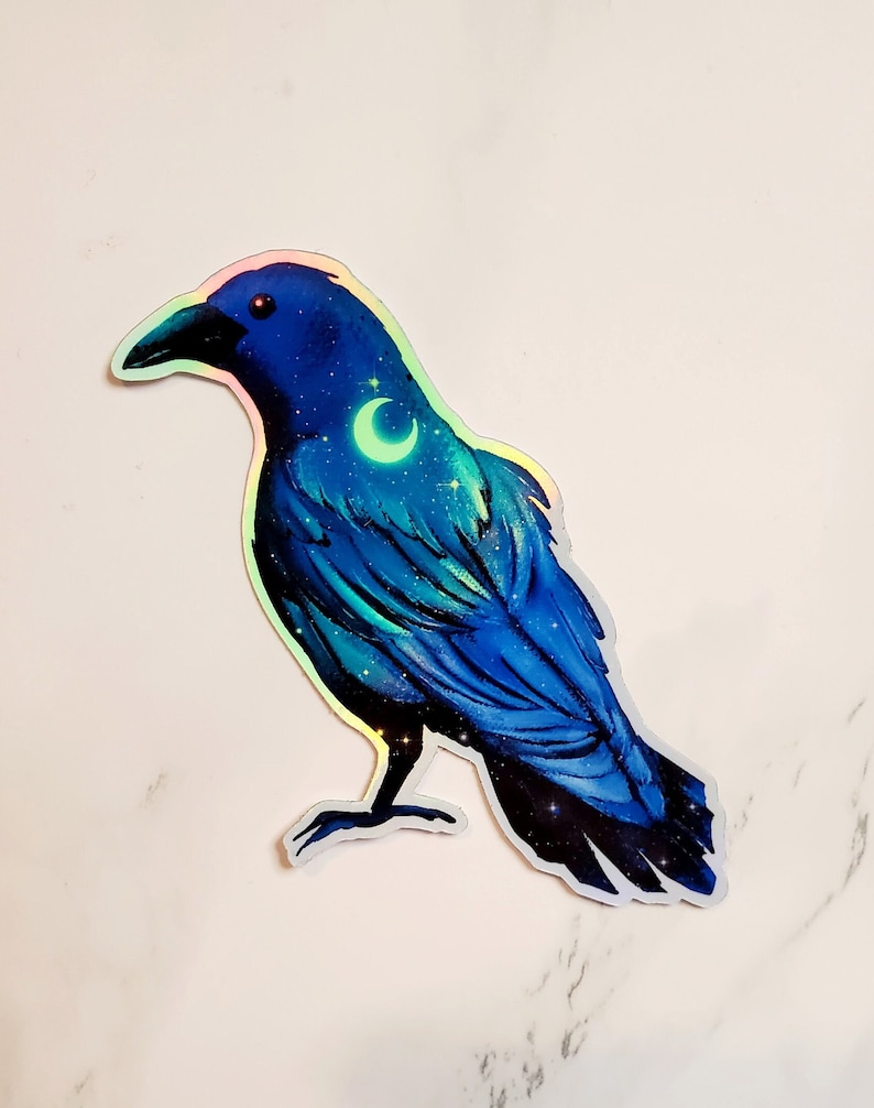May include: A blue iridescent sticker of a crow with a crescent moon and stars on its chest. The crow is standing on a white background.