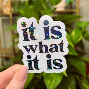 May include: A white sticker with iridescent glitter and black text that reads "it is what it is".