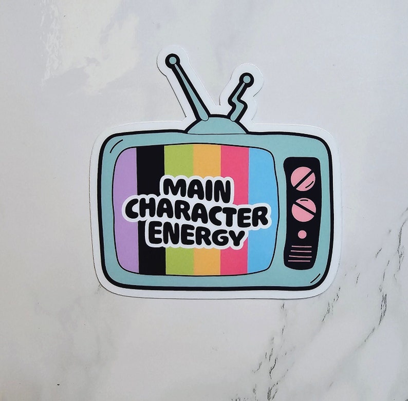 May include: A blue and white sticker featuring a cartoon television set. The television screen has a rainbow pattern and the text "Main Character Energy".