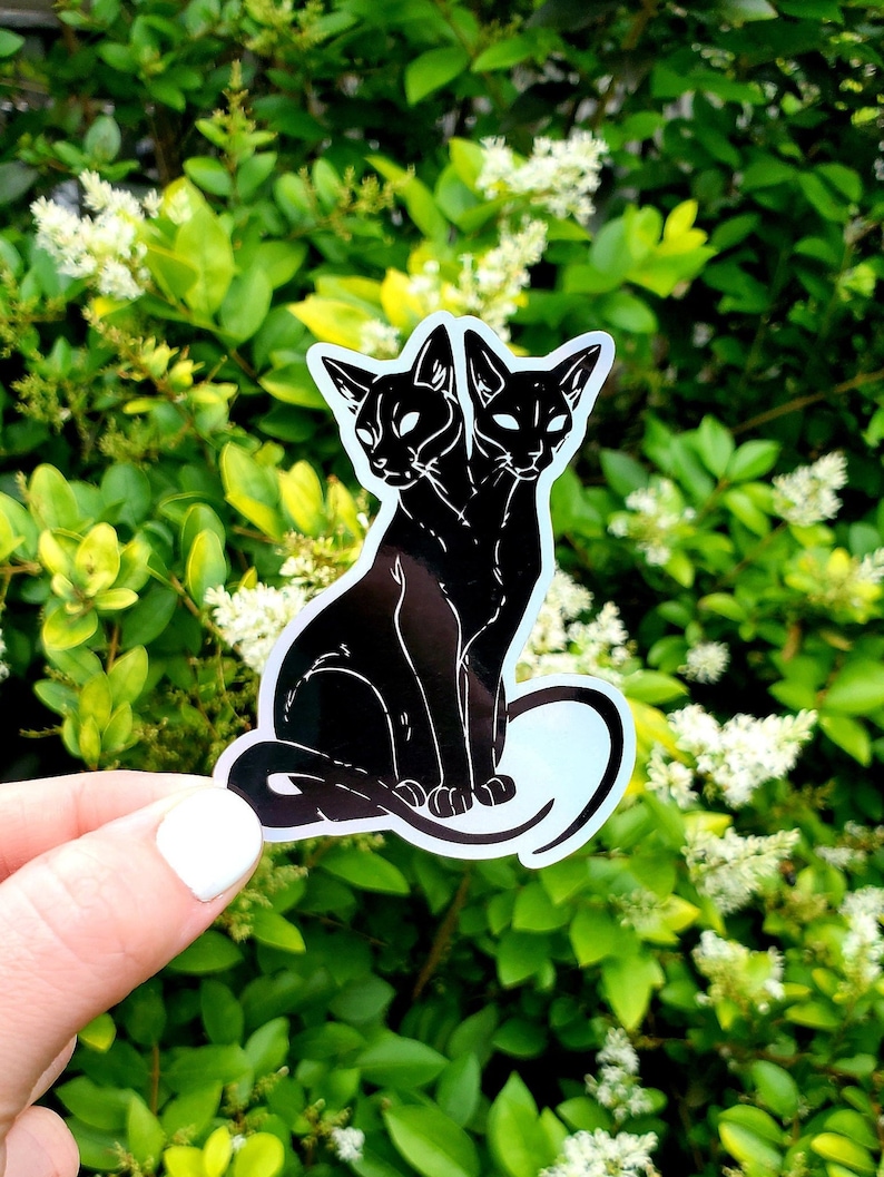 May include: Black and white sticker of a two-headed cat with a curled tail. The cat is sitting with its front paws together and its head tilted slightly to the side.