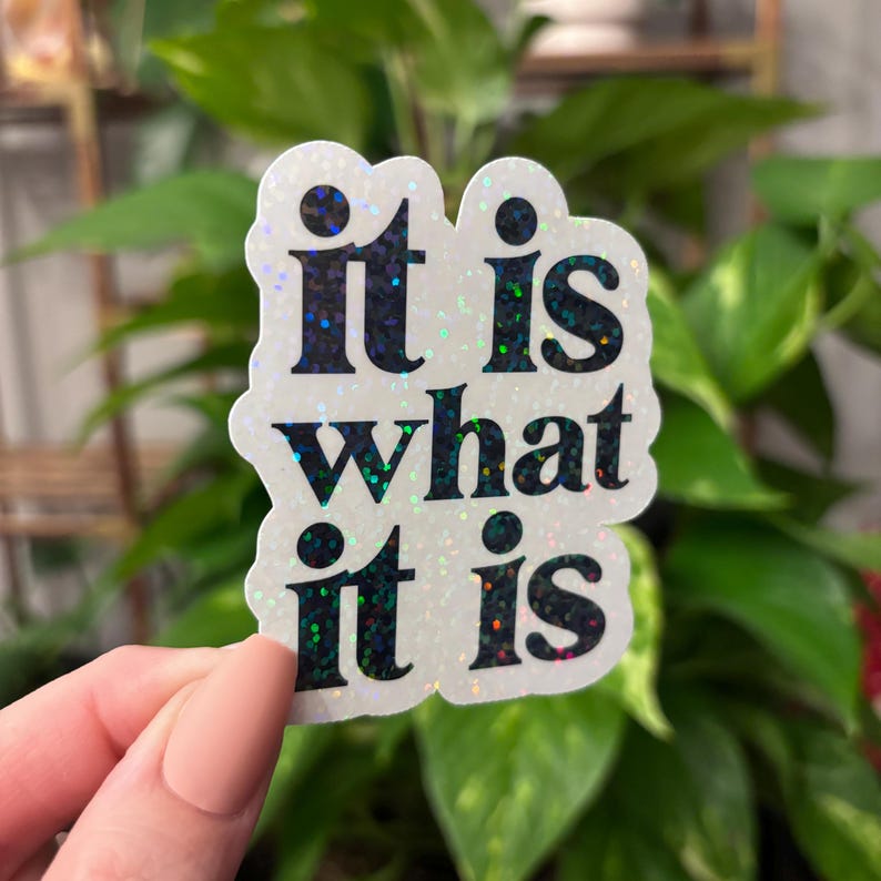 May include: A white sticker with iridescent glitter features the text "it is what it is" in black lettering.