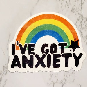 May include: A rainbow sticker with the text "I've got anxiety" in black lettering. The rainbow has a yellow, orange, red, green, blue, and purple colour scheme. There is a black star with a white outline in the top right corner of the sticker.