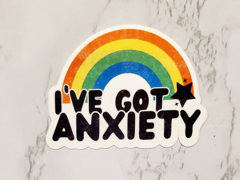 May include: A rainbow sticker with the text "I've got anxiety" in black lettering. The rainbow has a yellow, orange, red, green, blue, and purple colour scheme. There is a black star with a white outline in the top right corner of the sticker.