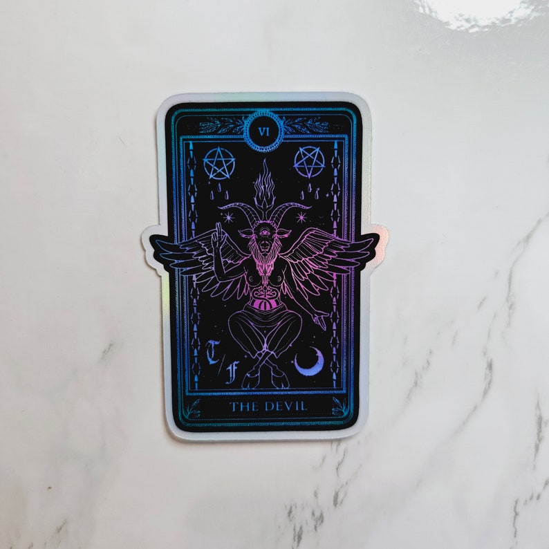 May include: A holographic sticker featuring a tarot card with the Devil, a horned figure with wings, and the text "THE DEVIL" at the bottom.