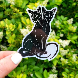 May include: A black and white sticker of a two-headed cat sitting with its tail curled around its body.