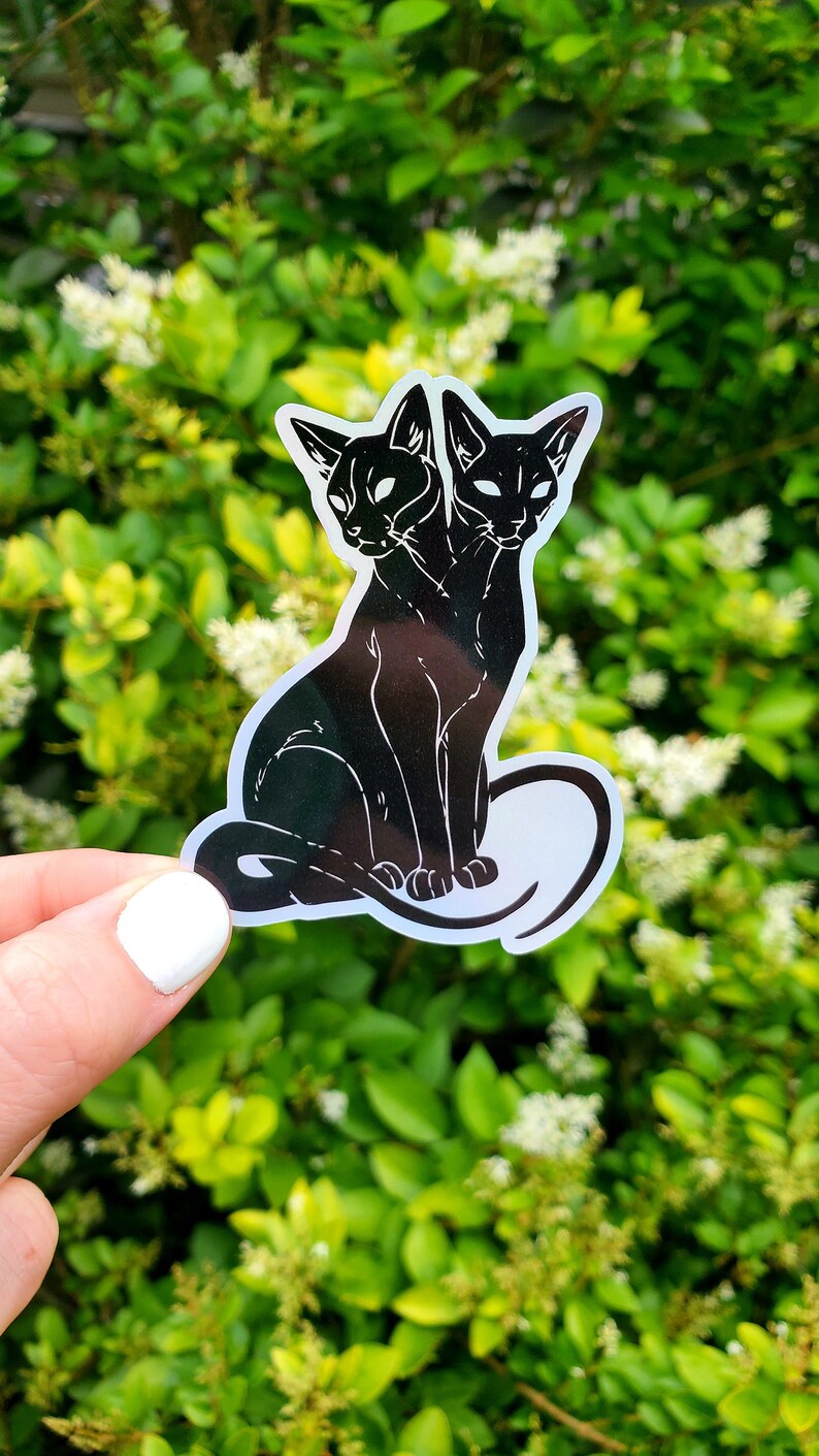 May include: A black and white sticker of a two-headed cat sitting with its tail curled around its body.