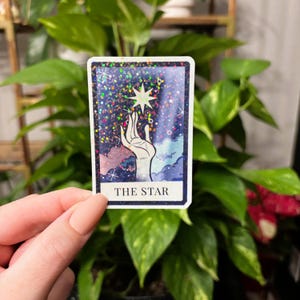 May include: A tarot card with a glittery background showing a hand reaching up to a star. The card is labelled "THE STAR".