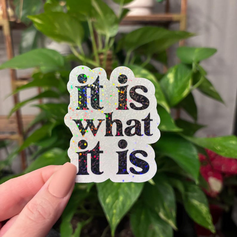 May include: A white sticker with iridescent glitter and black text that reads "it is what it is".