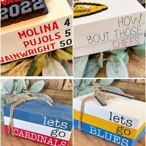 May include: Four wooden blocks stacked on top of each other, painted in red, white, and blue. The top block says "lets go cardinals" in black lettering.