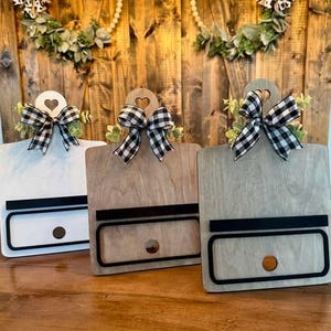 May include: Three wooden signs with a black and white checkered bow and a heart-shaped cutout at the top. Each sign has a black stripe and a cutout circle at the bottom.