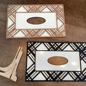 May include: Two wooden picture frames with a geometric pattern. The top frame is made of light wood and has a white background. The bottom frame is black and has a white background with a light shining through the cutouts. Both frames have an oval cutout in the center.