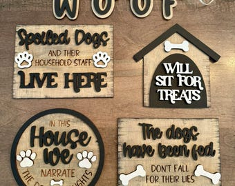 May include: Four wooden signs with dog-themed sayings. The signs are decorated with paw prints, bones, and the word "Woof" in a banner. The signs read: "Spoiled Dogs & Their Household Staff Live Here", "In This House We Narrate The Dog's Thoughts", "Will Sit For Treats", and "The Dogs Have Been Fed Don't Fall For Their Lies".