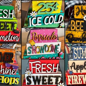 May include: A collection of decorative wooden signs with summer-themed phrases. Each sign features layered blocks with words like "Fresh," "Sweet," "Watermelon," and "Summer." Accents include bows, flowers, and sunglasses.