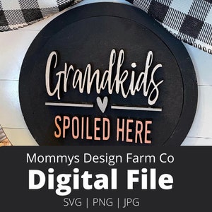 May include: A black and white round sign with the text "Grandkids Spoiled Here" in white and pink lettering. The sign has a heart shape in the middle. The sign is on a white wooden background.