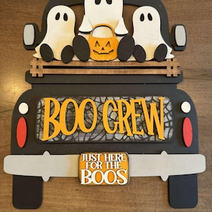 May include: A black wooden truck with a "BOO CREW" sign and three white ghosts on the back. The truck has a license plate that says "JUST HERE FOR THE BOOS".