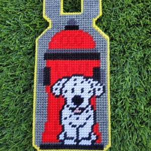 May include: A red fire hydrant with a black top and a white Dalmatian dog sitting in front of it. The fire hydrant and dog are embroidered on a gray fabric with a yellow border.