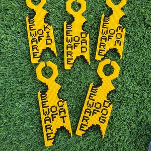 May include: Five yellow door hangers with black text that reads "BEWARE OF DOG", "BEWARE OF KID", and "BEWARE OF DAD". The hangers are made of a textured material and have a unique key-shaped design.