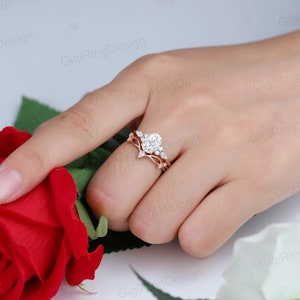 May include: A rose gold engagement ring set with a large round center stone and smaller accent stones. The ring is set on a delicate band with a floral design.