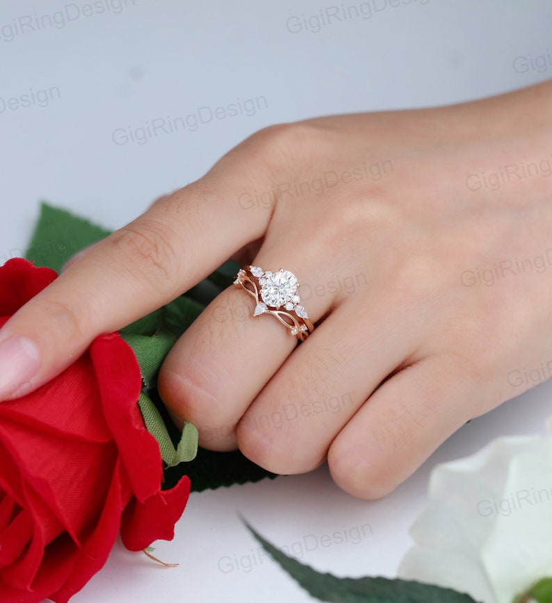 May include: A rose gold engagement ring set with a large round center stone and smaller accent stones. The ring is set on a delicate band with a floral design.