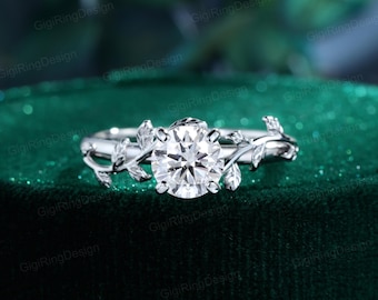 May include: A silver-toned ring featuring a central round-cut clear stone held by four prongs. The band is designed with a detailed vine and leaf motif that extends from the center setting along both sides of the polished metal ring shank.