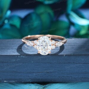 May include: A rose gold engagement ring with an oval-shaped center stone and pear-shaped accent stones. The ring is set on a white background.