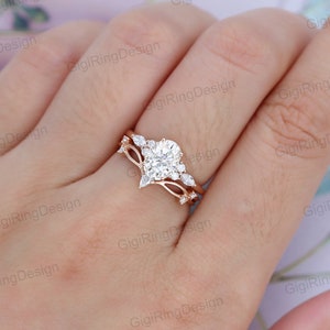 May include: A rose gold engagement ring set with a large oval-shaped center stone and smaller pear-shaped accent stones. The ring is set on a delicate band with a delicate, curved design.