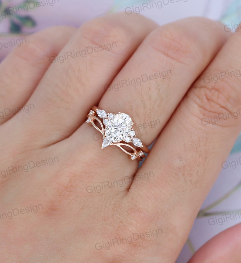 May include: A rose gold engagement ring set with a large oval-shaped center stone and smaller pear-shaped accent stones. The ring is set on a delicate band with a delicate, curved design.