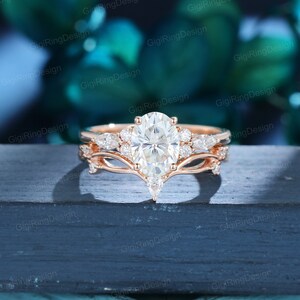 May include: A rose gold engagement ring set with a large oval-shaped center stone and smaller pear-shaped accent stones. The ring is set on a delicate band with a delicate, curved design.