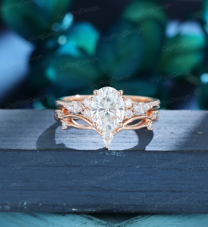 May include: A rose gold engagement ring set with a large oval-shaped center stone and smaller pear-shaped accent stones. The ring is set on a delicate band with a delicate, curved design.