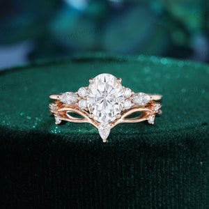 May include: A rose gold engagement ring set with a large oval-shaped center stone and smaller pear-shaped accent stones. The ring is set on a green velvet background.