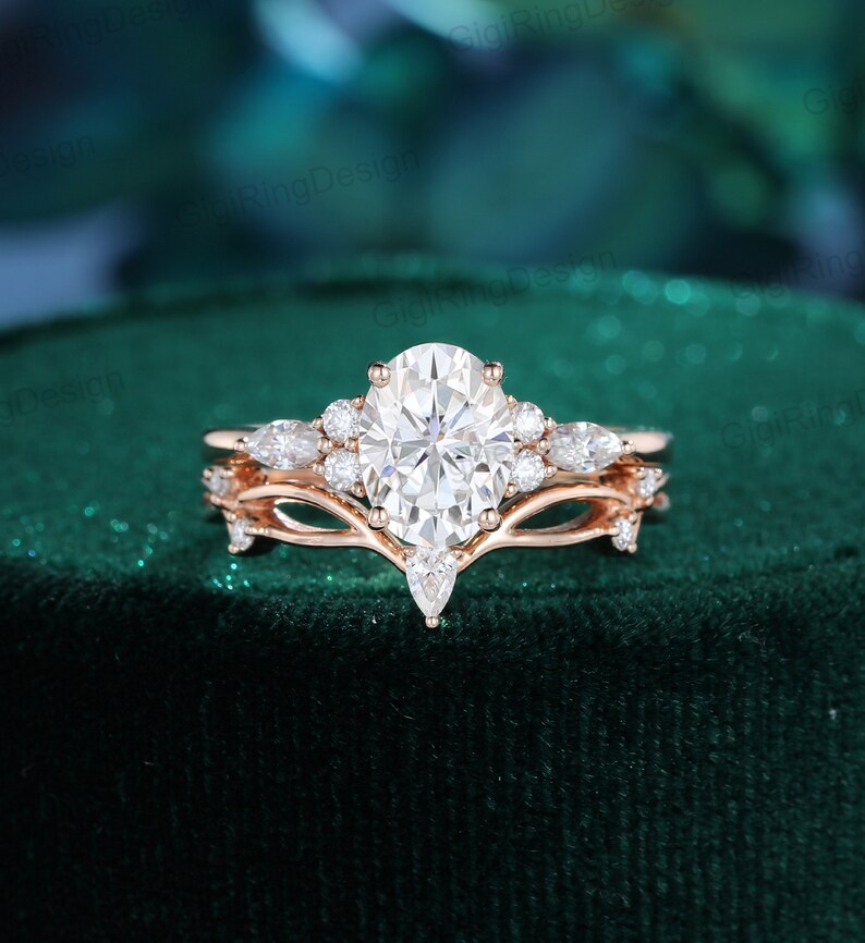 May include: A rose gold engagement ring set with a large oval-shaped center stone and smaller pear-shaped accent stones. The ring is set on a green velvet background.