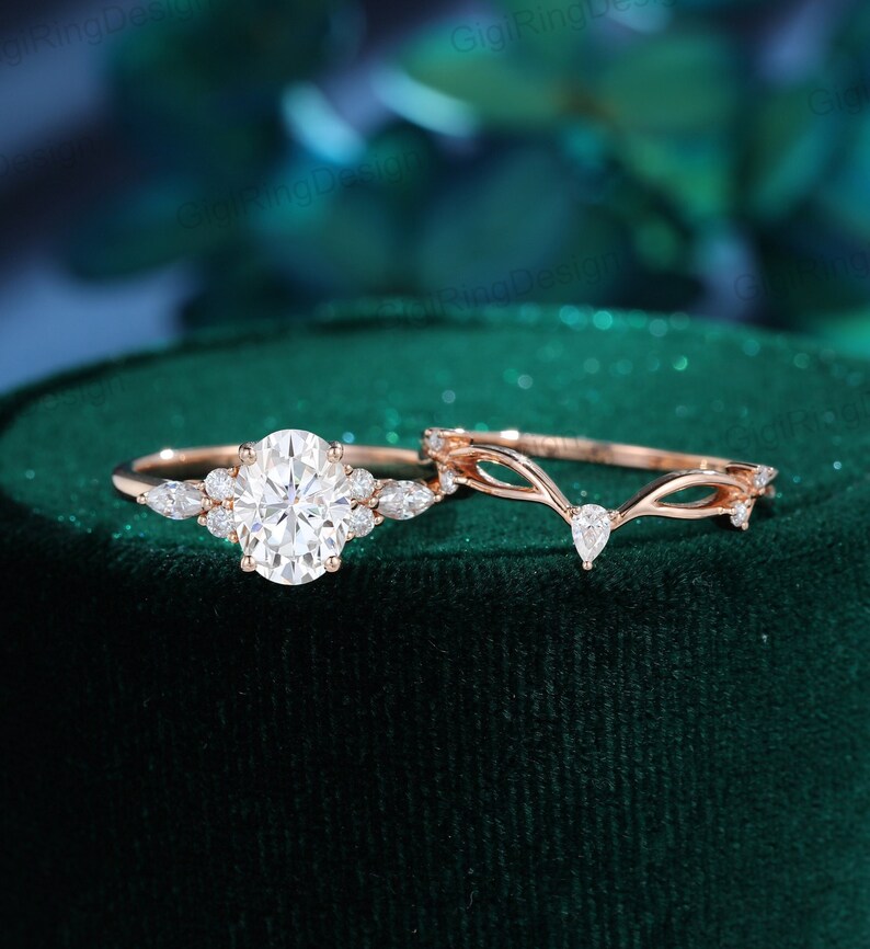 May include: A rose gold engagement ring set with a large oval-shaped center stone and smaller pear-shaped accent stones. The matching wedding band features a delicate, curved design with small accent stones.