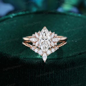 May include: A rose gold engagement ring set featuring a central marquise-cut stone surrounded by smaller marquise and round-cut stones. The set includes a matching V-shaped band adorned with round-cut stones, creating a layered, multi-stone design.