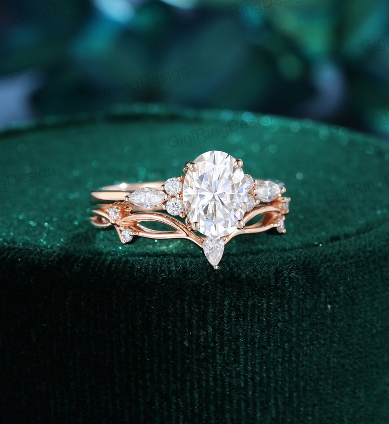 May include: A rose gold engagement ring set with a large oval-shaped center stone and smaller pear-shaped accent stones. The ring band features a delicate vine design with small leaves.