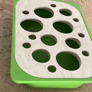Könnte beinhalten: Ein grünes Tablett mit einem Holzeinsatz mit mehreren runden Ausschnitten in verschiedenen Größen. Das Tablett ist aus Kunststoff und hat eine glatte, glänzende Oberfläche.
