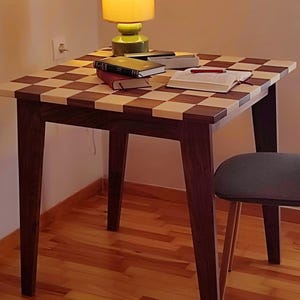 Könnte beinhalten: Kleiner Holztisch mit Schachbrettmuster, dunkelbraunen Beinen und passendem Stuhl. Bücher, ein Stift und eine Lampe stehen auf dem Tisch. Der Tisch ist ca. 76 cm lang und breit.