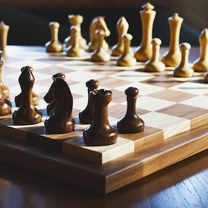 May include: A wooden chessboard with black and white squares. The board is set up with black and white chess pieces. The pieces are arranged in a traditional starting position.