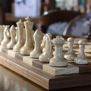 May include: A wooden chess set with light brown pieces on a wooden board. The pieces are arranged in a starting position for a game of chess.