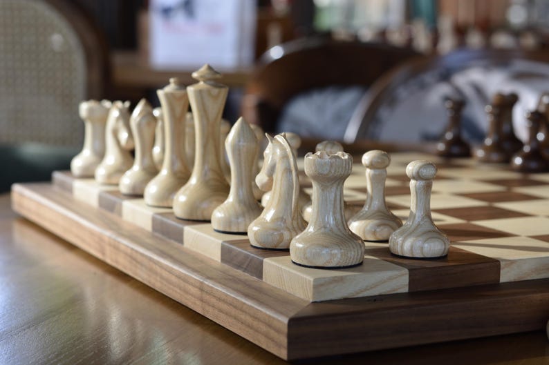 May include: A wooden chess set with light brown pieces on a wooden board. The pieces are arranged in a starting position for a game of chess.