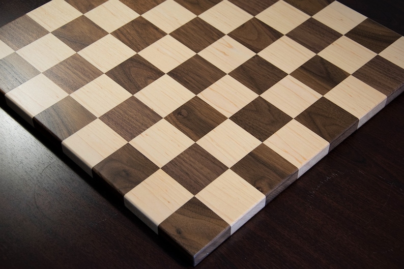 May include: A wooden chessboard with alternating squares of light brown maple and dark brown walnut wood.