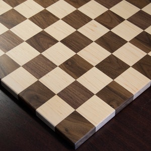 May include: A wooden chessboard with alternating squares of light brown and dark brown wood.