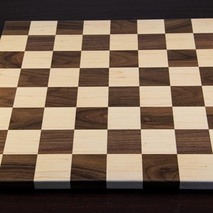 May include: A wooden chessboard with alternating squares of light brown and dark brown wood.