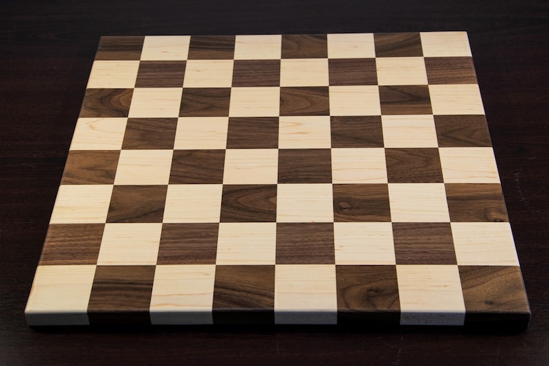 May include: A wooden chessboard with alternating squares of light brown and dark brown wood.