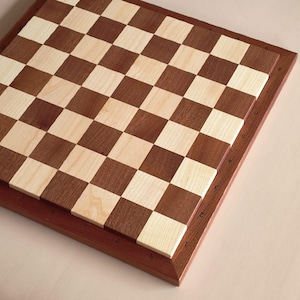 May include: A wooden chess board with a checkerboard pattern of light and dark brown squares. The board is framed in a darker wood, with numbers and letters along the edges.