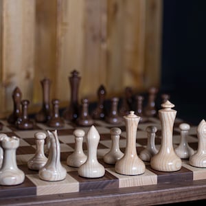 May include: A wooden chess set with light and dark brown pieces on a wooden board with a light and dark brown checkered pattern.